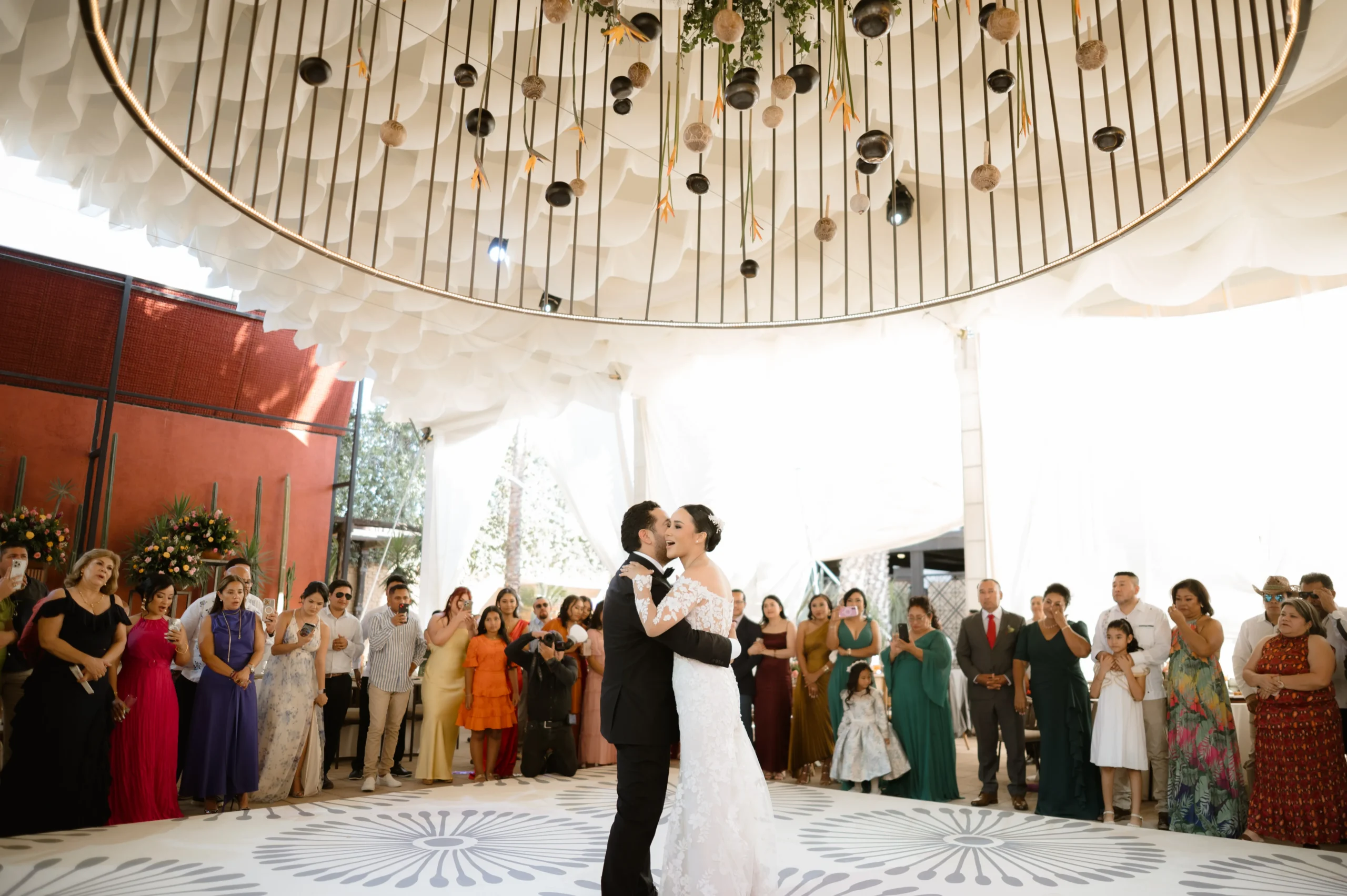 Boda multicultural: Fotografía de una pareja de novios abrazados mientras están de pie y alrededor los invitados.